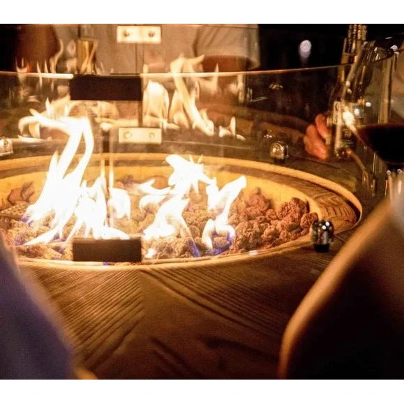 Elementi Lafite Barrel Bar fire table with circular glass-enclosed fire pit, glowing flames, dark fuel, and wooden base