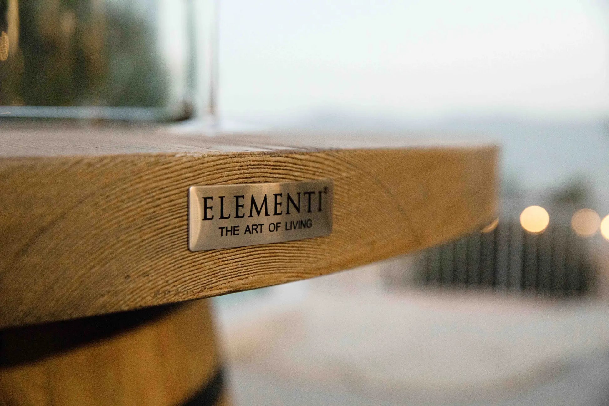 Light brown wooden table with metallic plaque engraved elementi the art of living on Elementi Lafite Barrel Bar Fire Table 13.2 kW