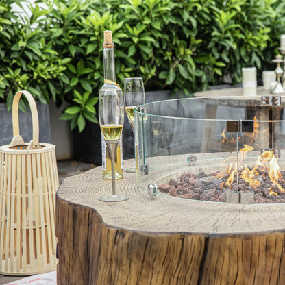 Elementi Manchester fire table with clear glass fire pit and circular cover featuring glowing flames over volcanic rocks