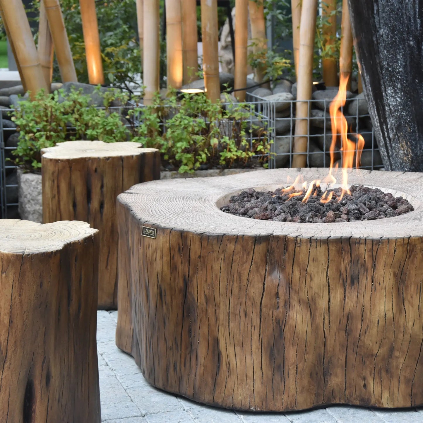 Elementi Manchester fire table featuring rustic wooden fire pit from single tree trunk with charred edges and glowing flames