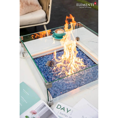 Elementi Plus Bianco fire table with square glass top, blue glass beads, central flame, and metallic edges