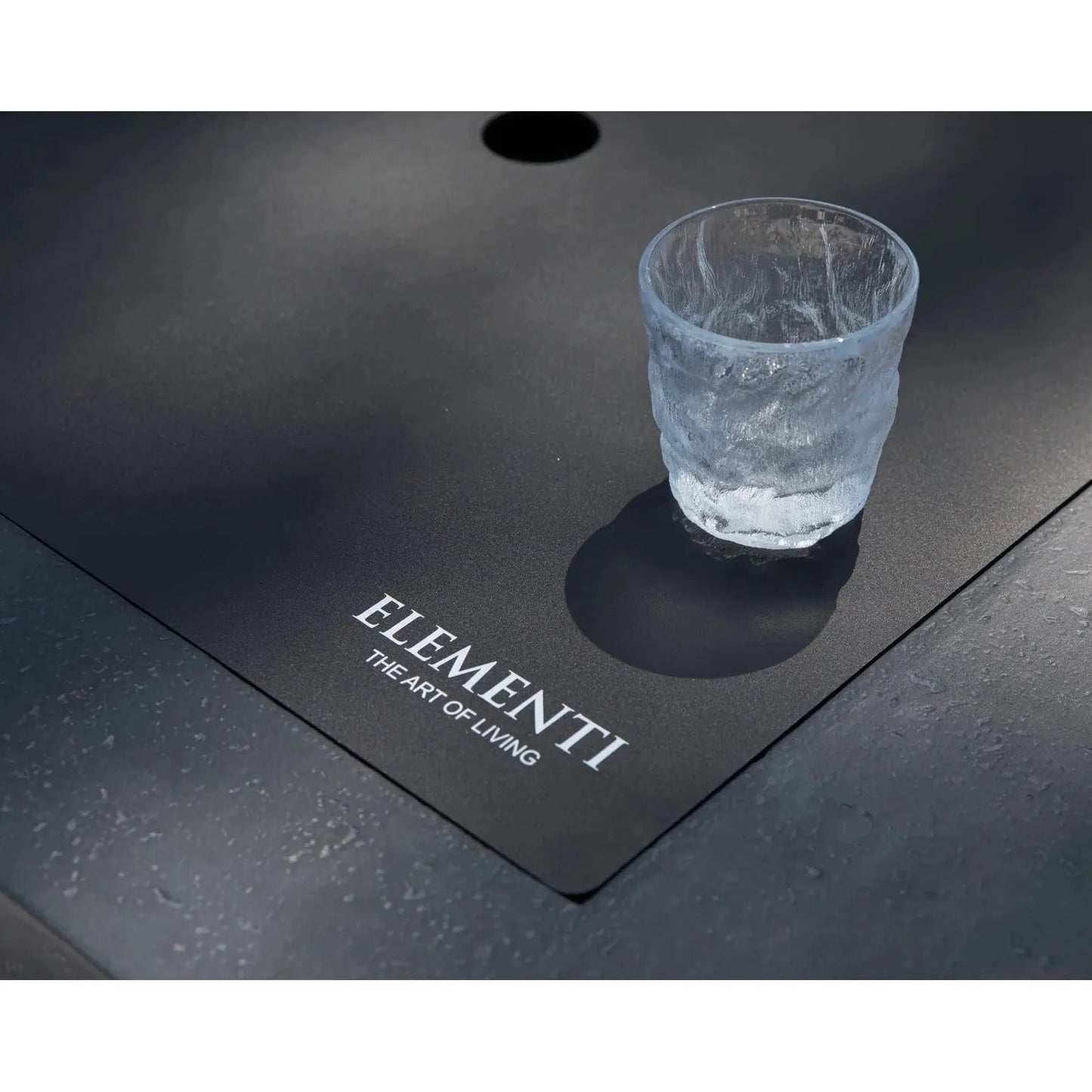 A clear textured glass tumbler with frosted finish on a sleek black surface beside elementi plus cannes fire table 16 kW