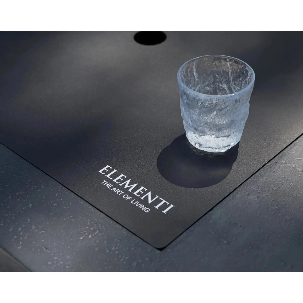 A clear textured glass tumbler with frosted finish on a sleek black surface beside elementi plus cannes fire table 16 kW