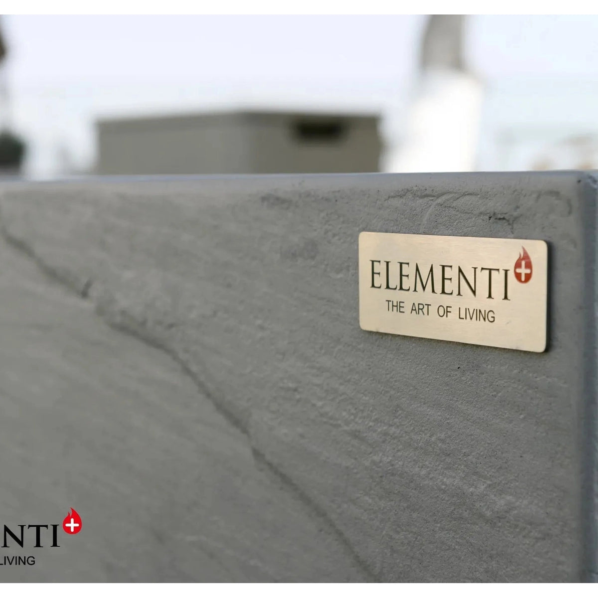 A sleek matte gray ceramic tile with natural stone texture and a brass elementi plaque for the elementi plus capertee fire table