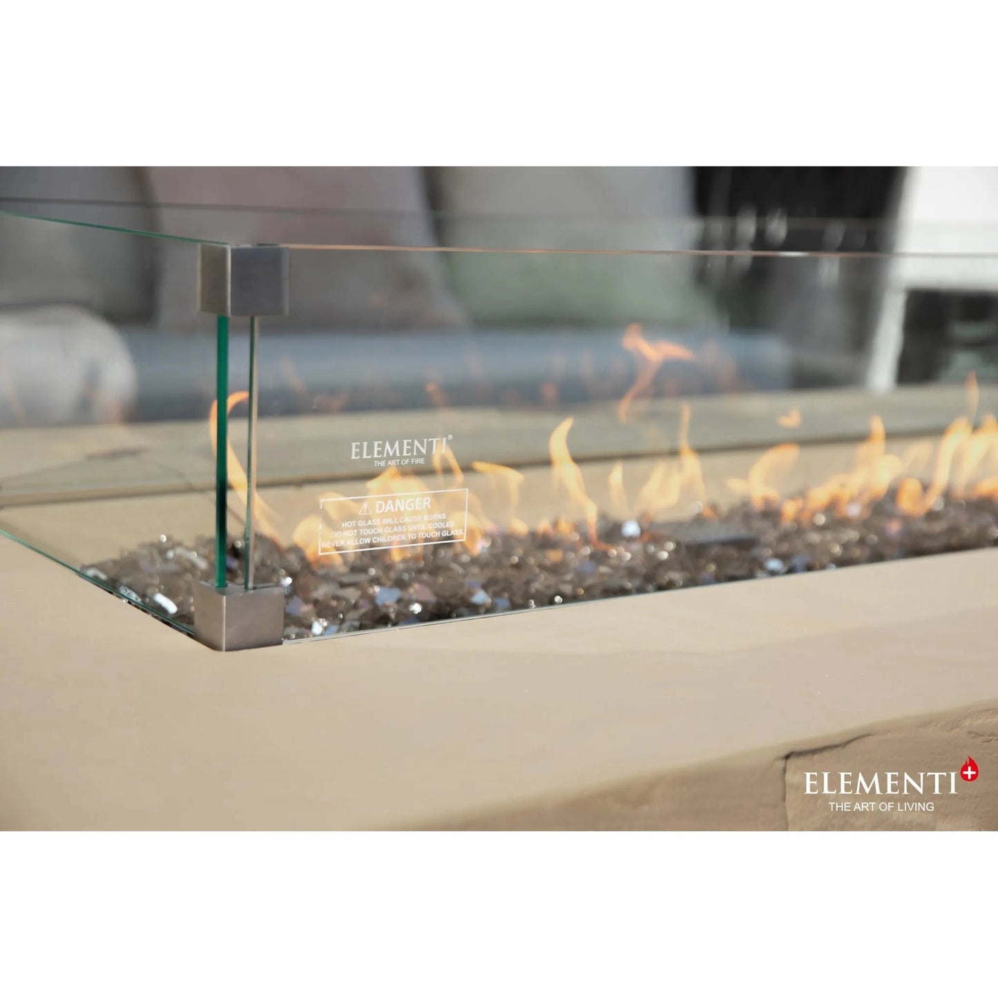 Elementi Plus Colorado fire table with modern glass enclosure, sleek metallic frame, and glowing orange flames over gray pebbles