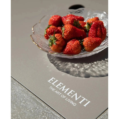 A clear textured glass bowl with a gold rim holding red strawberries complements the elementi plus monte carlo fire table 16 kw