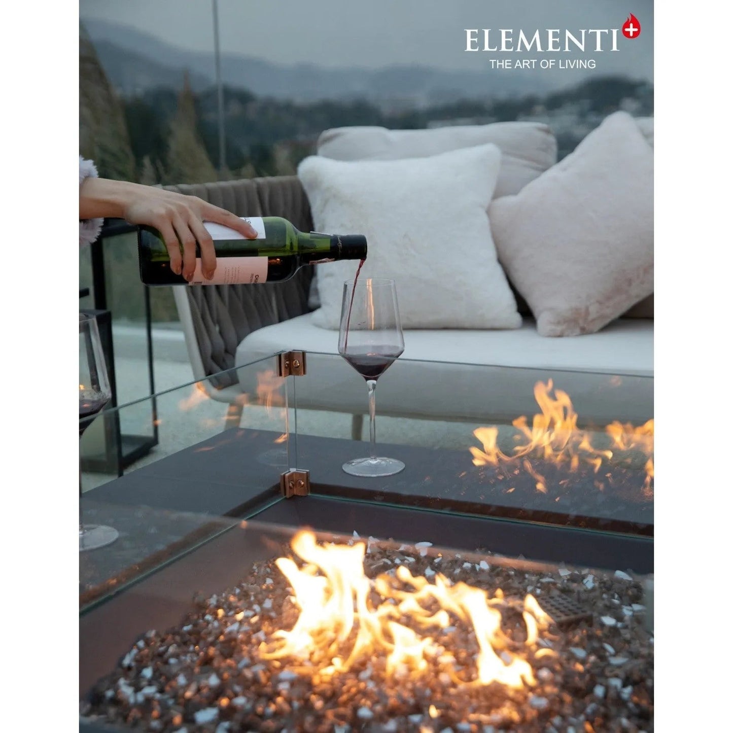 Dark green glass wine bottle with white label being poured into clear stemmed wineglass near elementi plus roraima fire table 16 kw