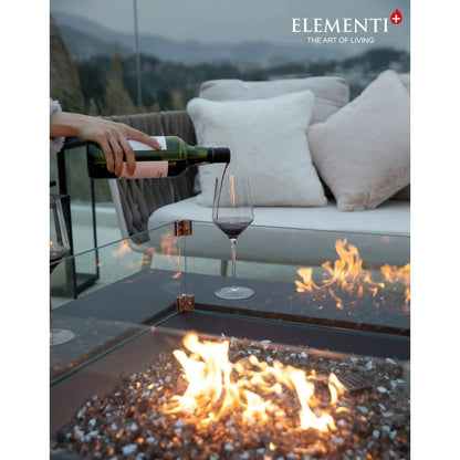 Dark green glass wine bottle with white label being poured into clear stemmed wineglass near elementi plus roraima fire table 16 kw