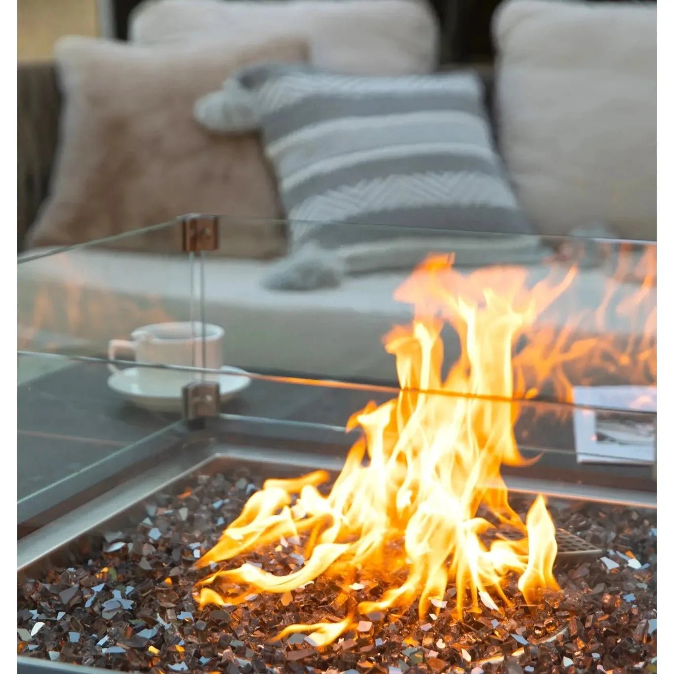 Elementi Plus Sofia fire table with square glass top and flickering orange flames over dark reflective glass pebbles