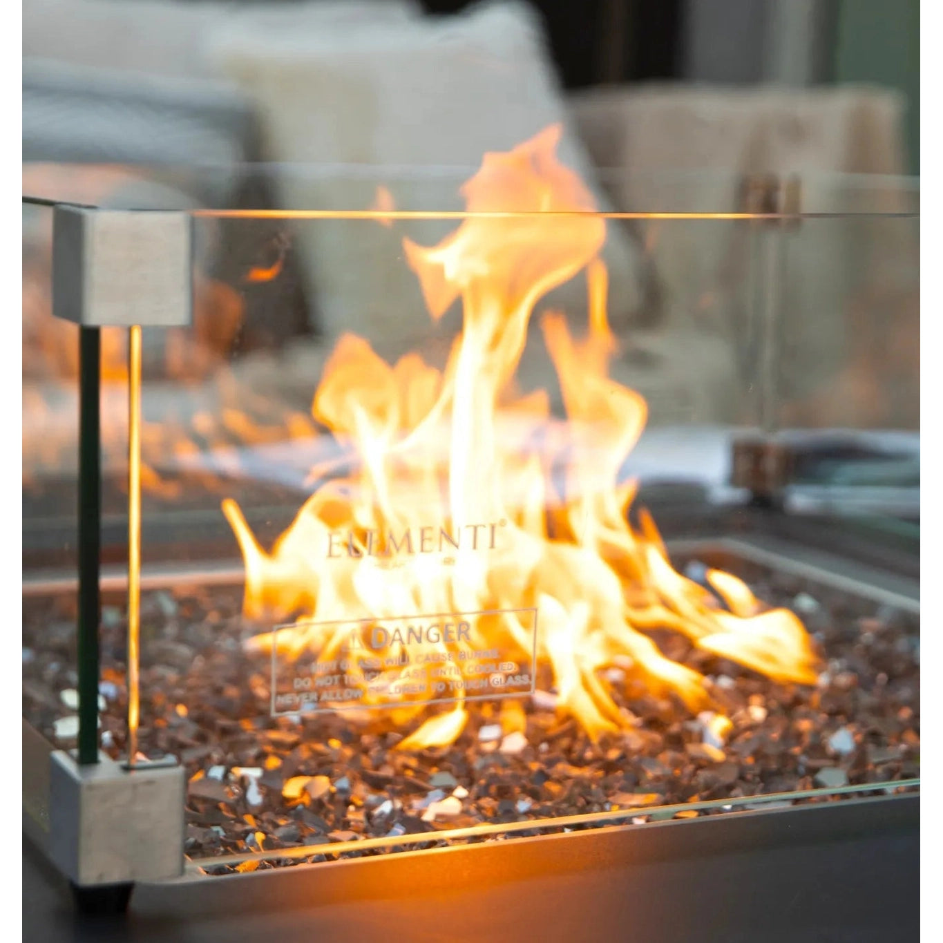 Elementi Plus Sofia fire table with a glass enclosure and metallic frame featuring vibrant orange flames on pebbles