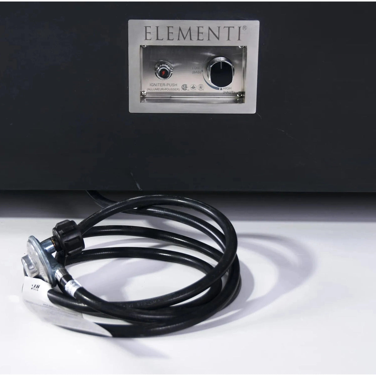 Black coiled gas hose with metallic connector and white label in front of elementi silver control panel for fire table