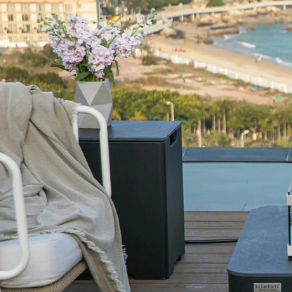 Elementi plus tank cover in black porcelain shown with a geometric gray ceramic vase holding light purple flowers