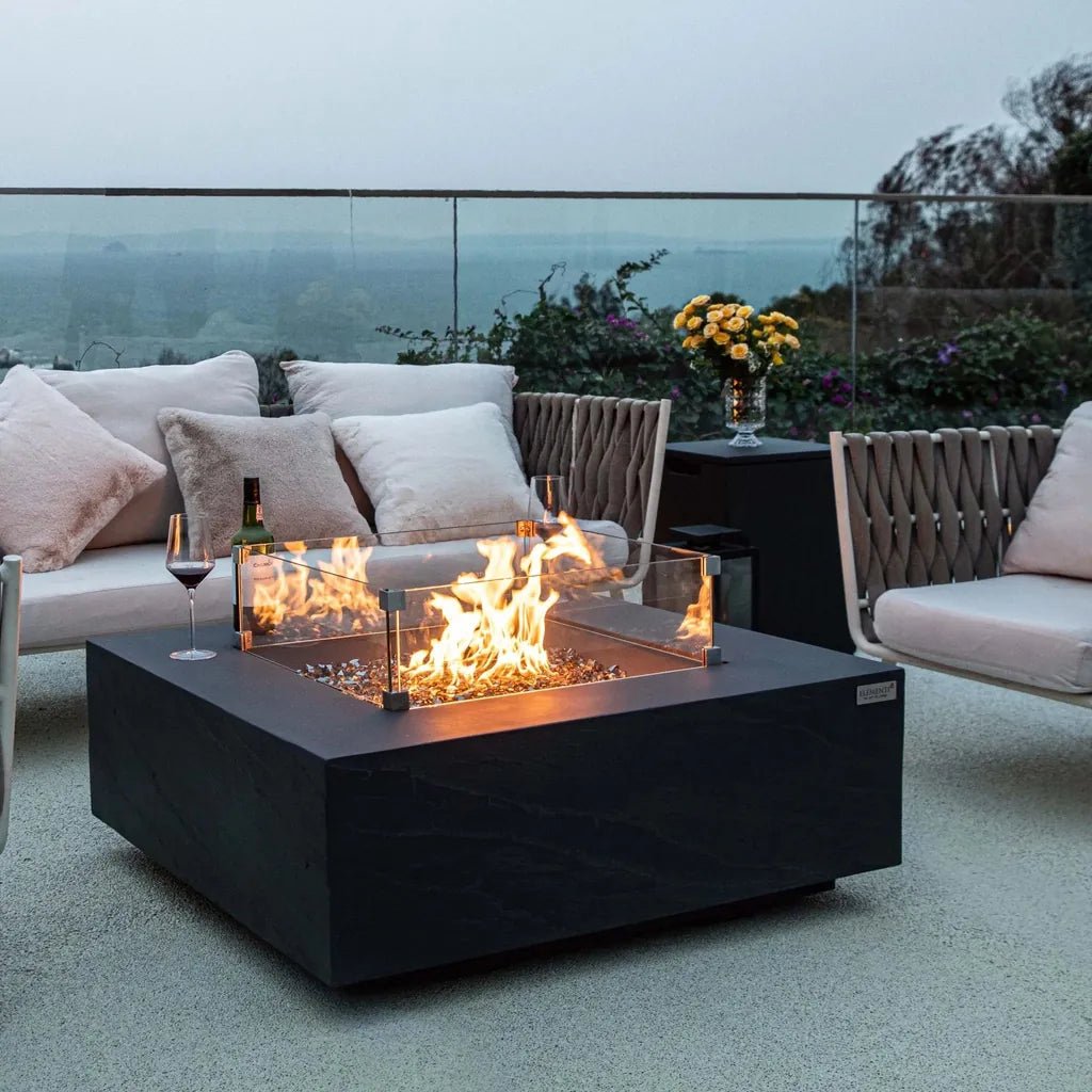 Black square fire pit with glass sides and glowing orange flames featuring elementi plus tank cover slate black onb404sl