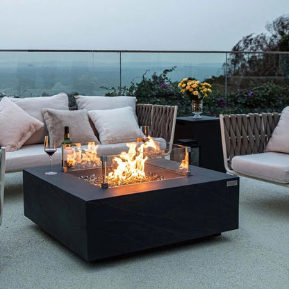 Black square fire pit with glass sides and glowing orange flames featuring elementi plus tank cover slate black onb404sl