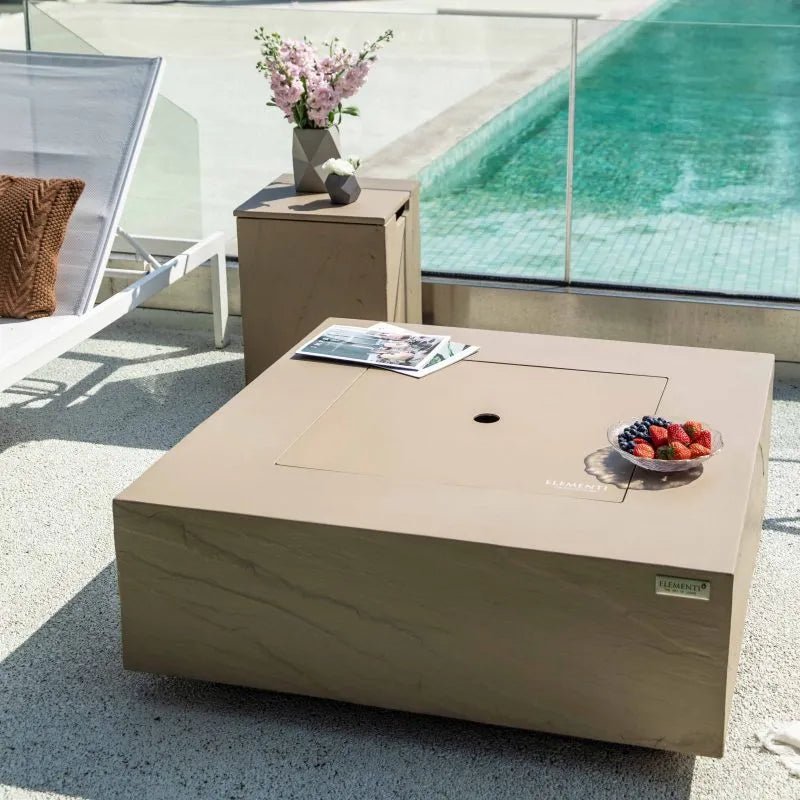 Beige stone-effect outdoor coffee table with central fire pit opening and small bowl of fruit on top sunlight yellow tank cover