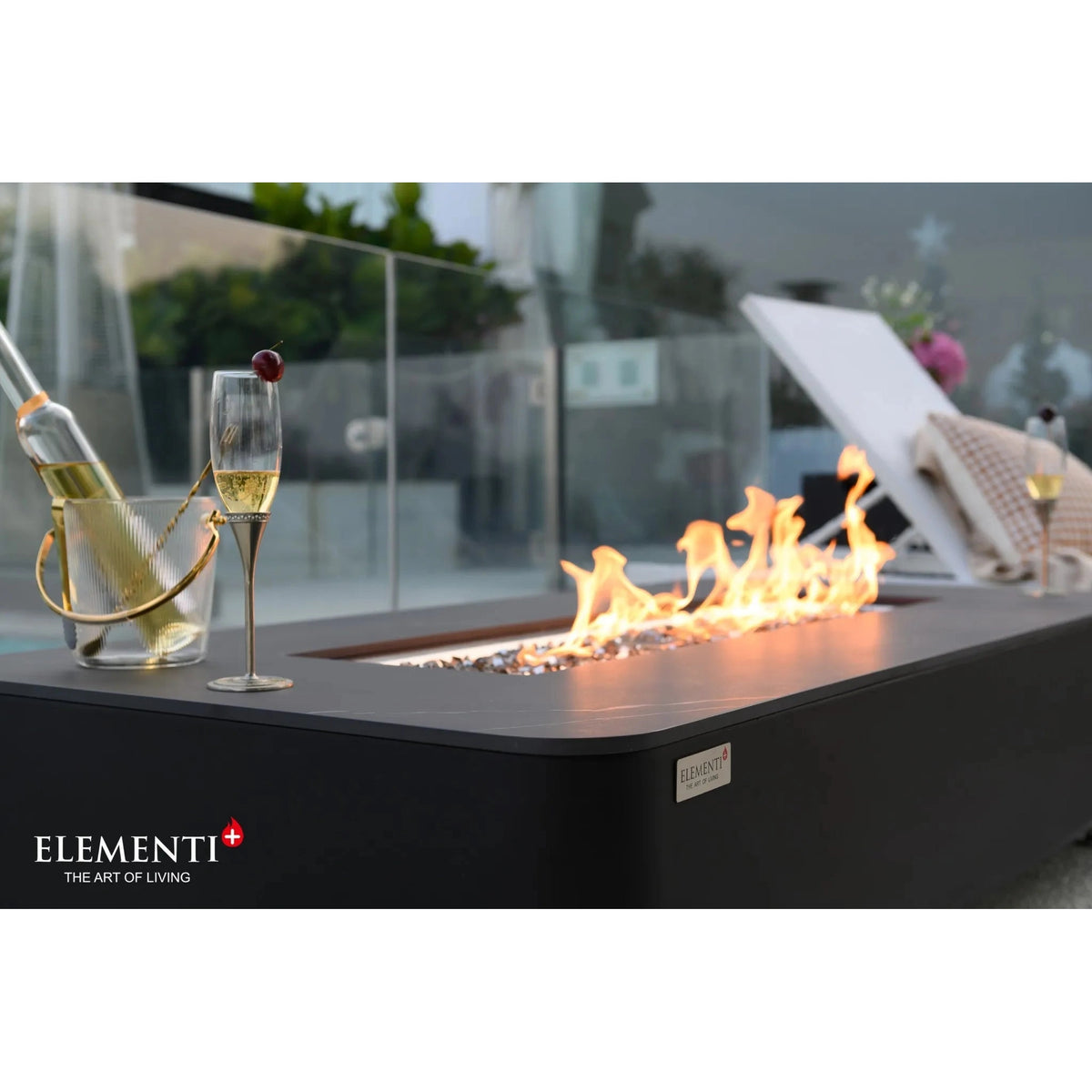 Black rectangular Elementi Plus Valencia fire table with 16 kW flames and a champagne bottle in an ice bucket nearby