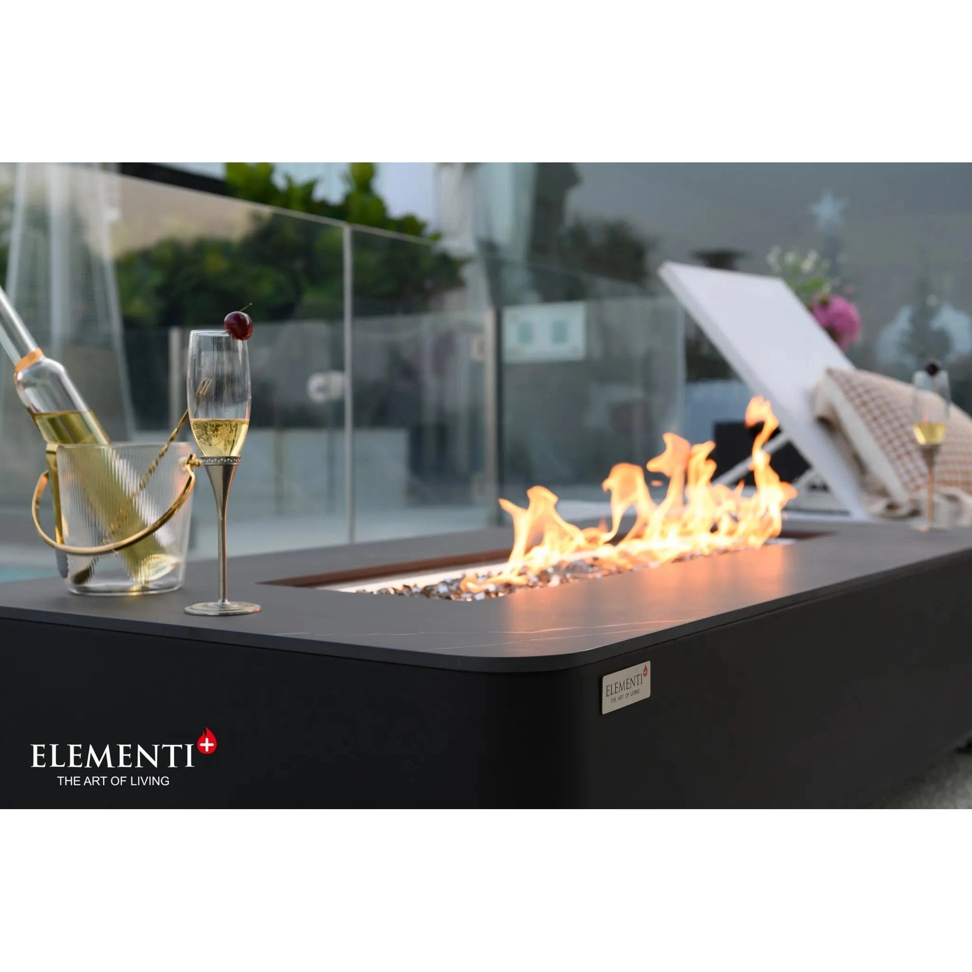 Black rectangular Elementi Plus Valencia fire table with 16 kW flames and a champagne bottle in an ice bucket nearby
