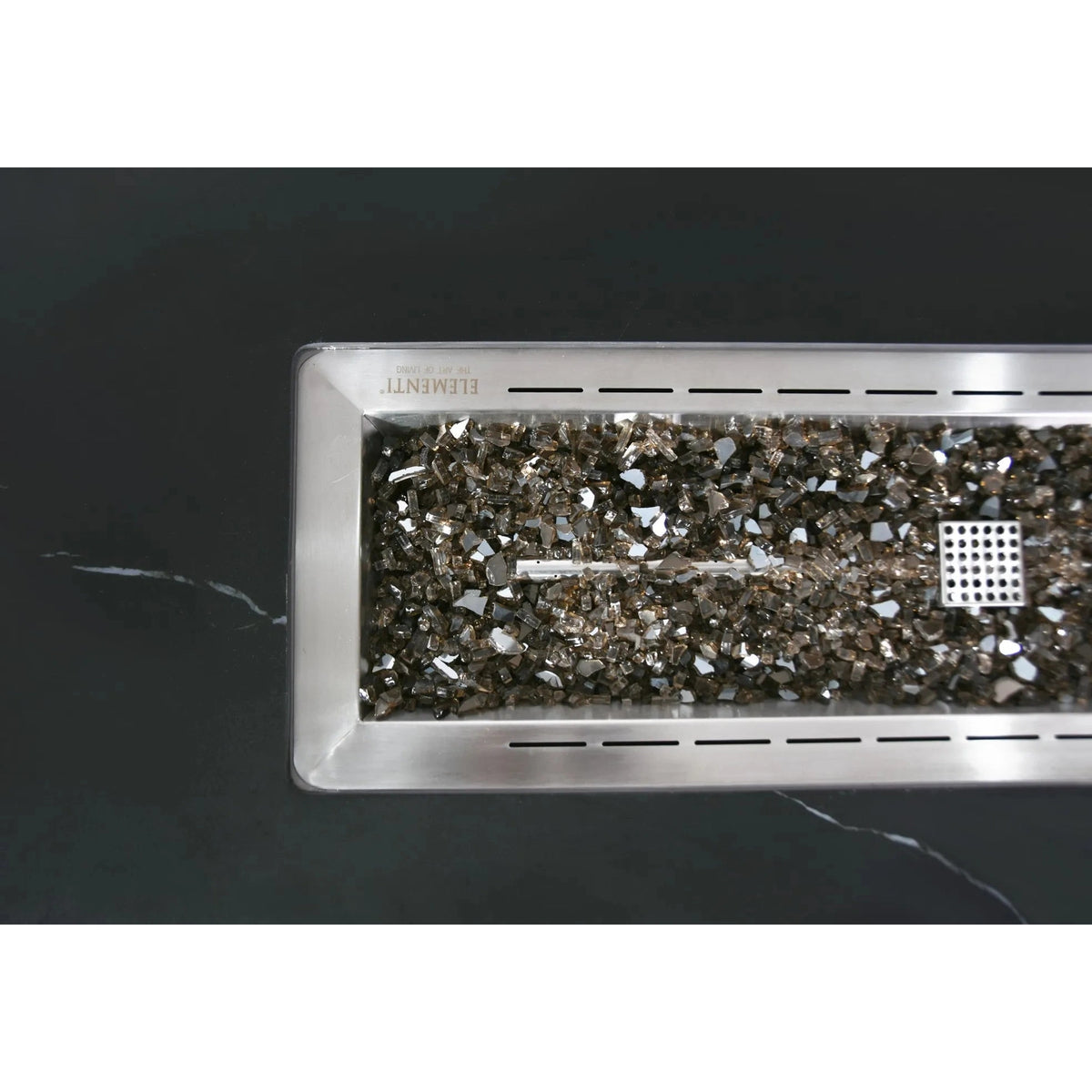 Rectangular stainless steel fire pit insert filled with reflective metallic glass shards in elementi plus varna fire table