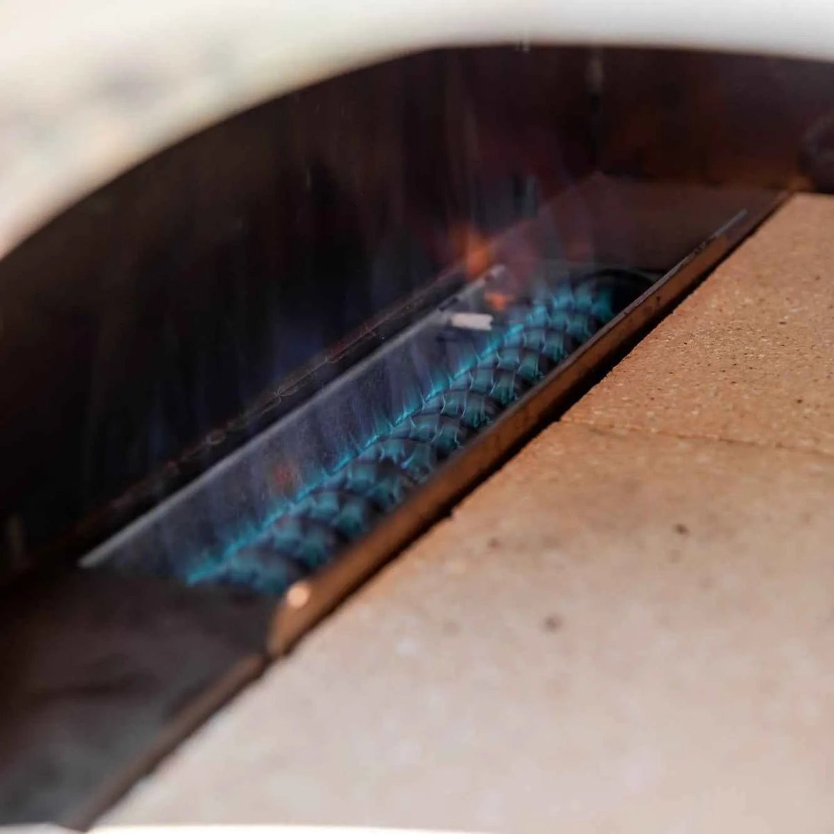 Blue gas flames burn along metal burner grate inside anthracite fontana margherita dual fuel outdoor pizza oven