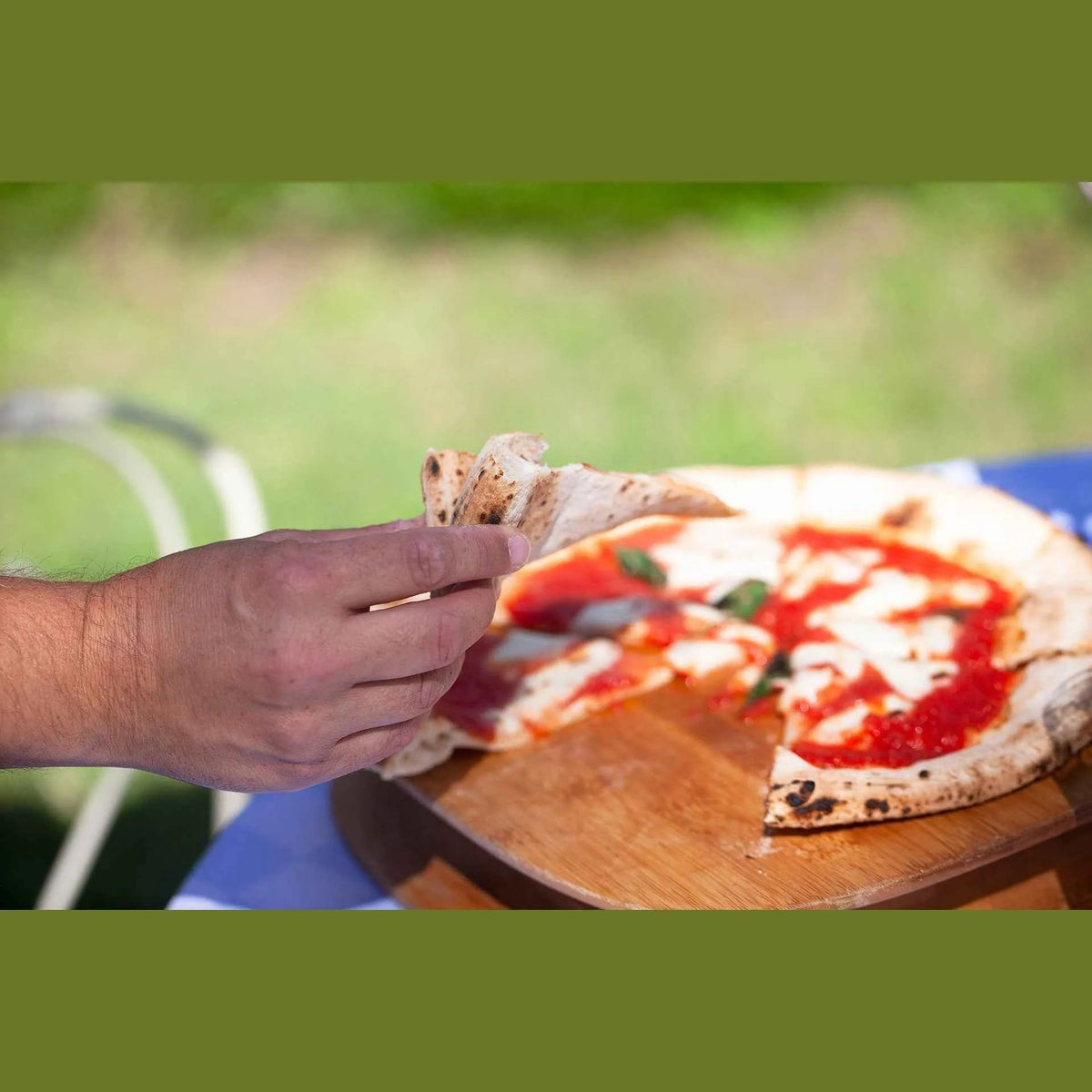 A hand holding a thin crust pizza slice with charred edges and basil made in a fontana marinara anthracite pizza oven
