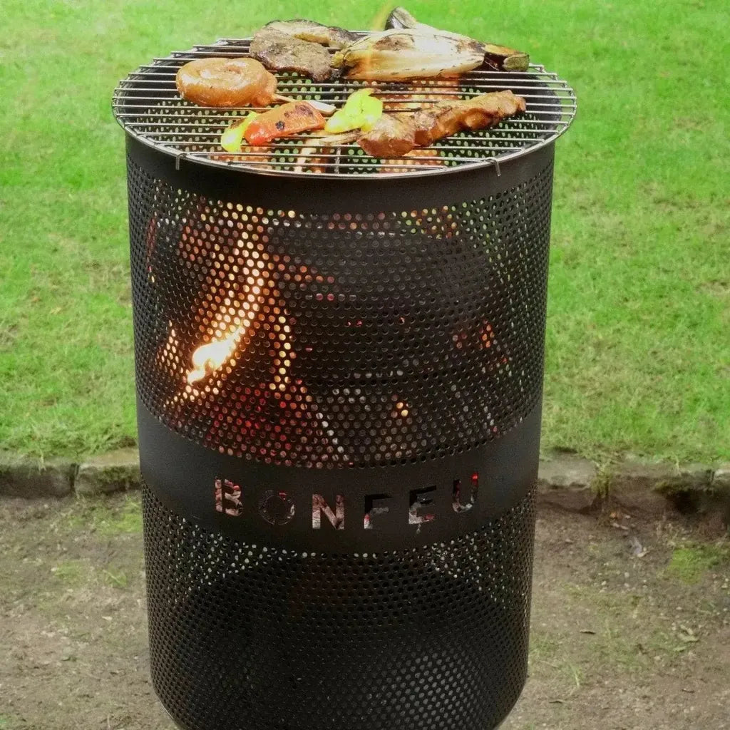 Black perforated metal BonFeu BonVes 34 fire pit with wire rack grilling meats and vegetables over glowing embers