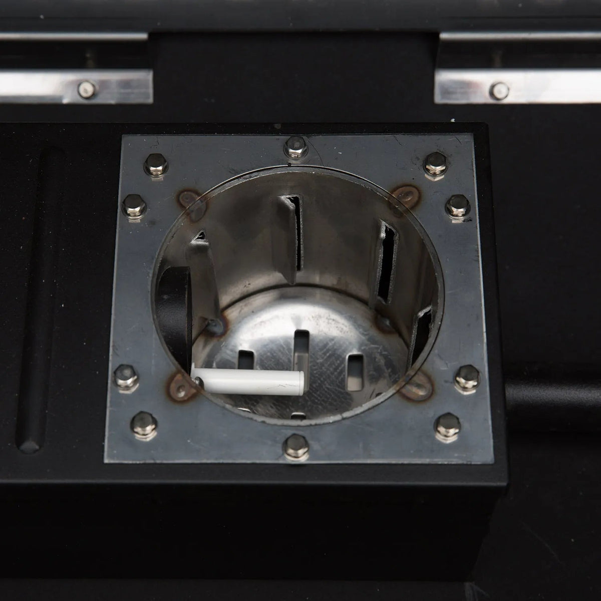 A white cylindrical cigarette resting inside a metallic receptacle of the gmg ledge prime plus wiFi pellet grill smoker