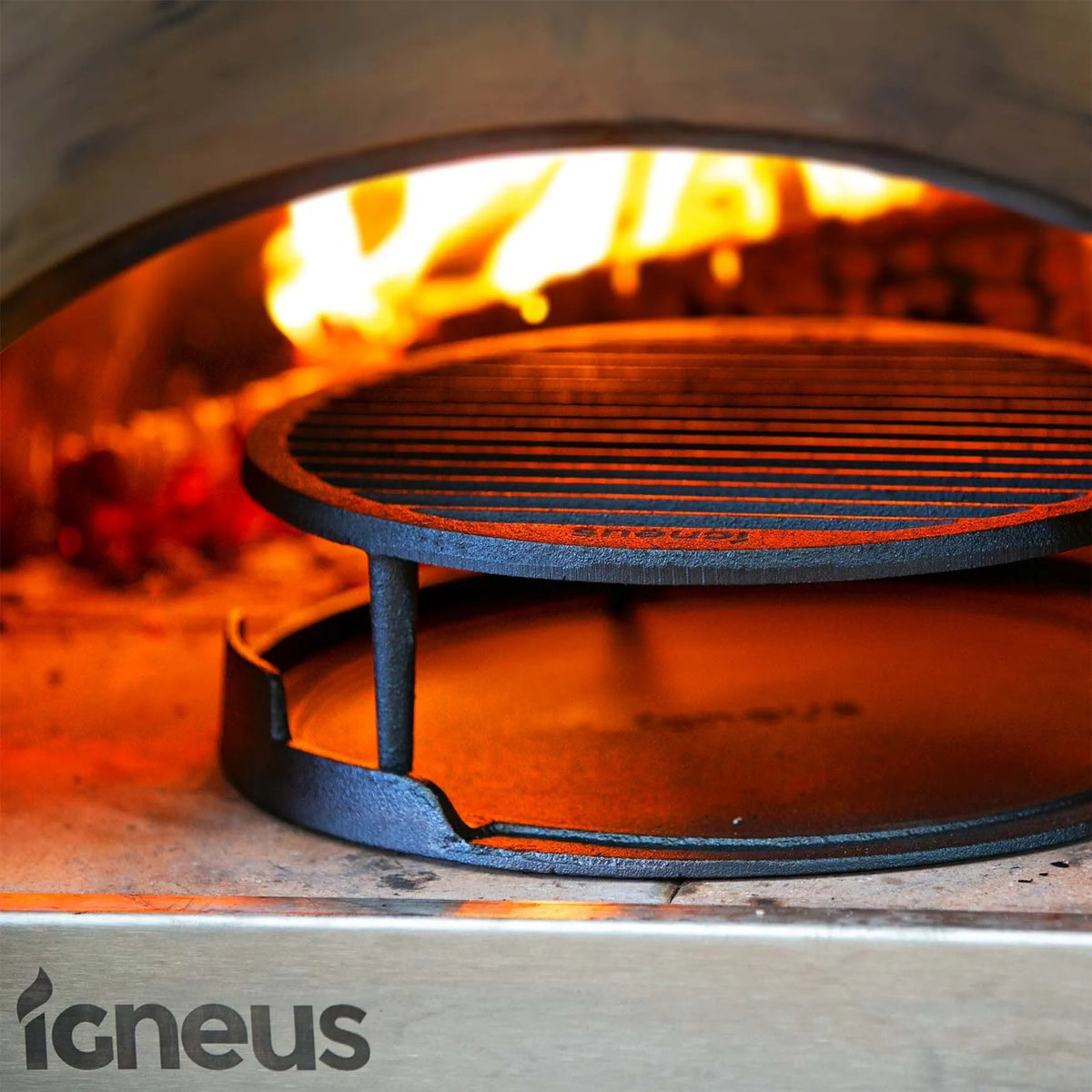 Black cast iron igneus tuscan grill rack with parallel ridges inside a glowing fire pizza oven cooking grate