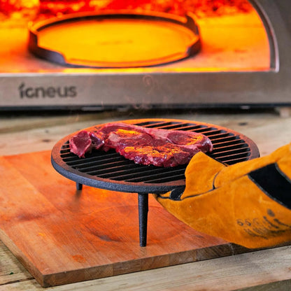 Igneus cast iron tuscan grill black cast iron grate with three legs holding seasoned raw steak for pizza oven cooking