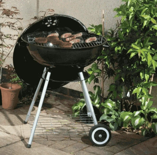 Lifestyle 22 kettle charcoal bbq in black with silver legs and a round cooking grate holding sausages