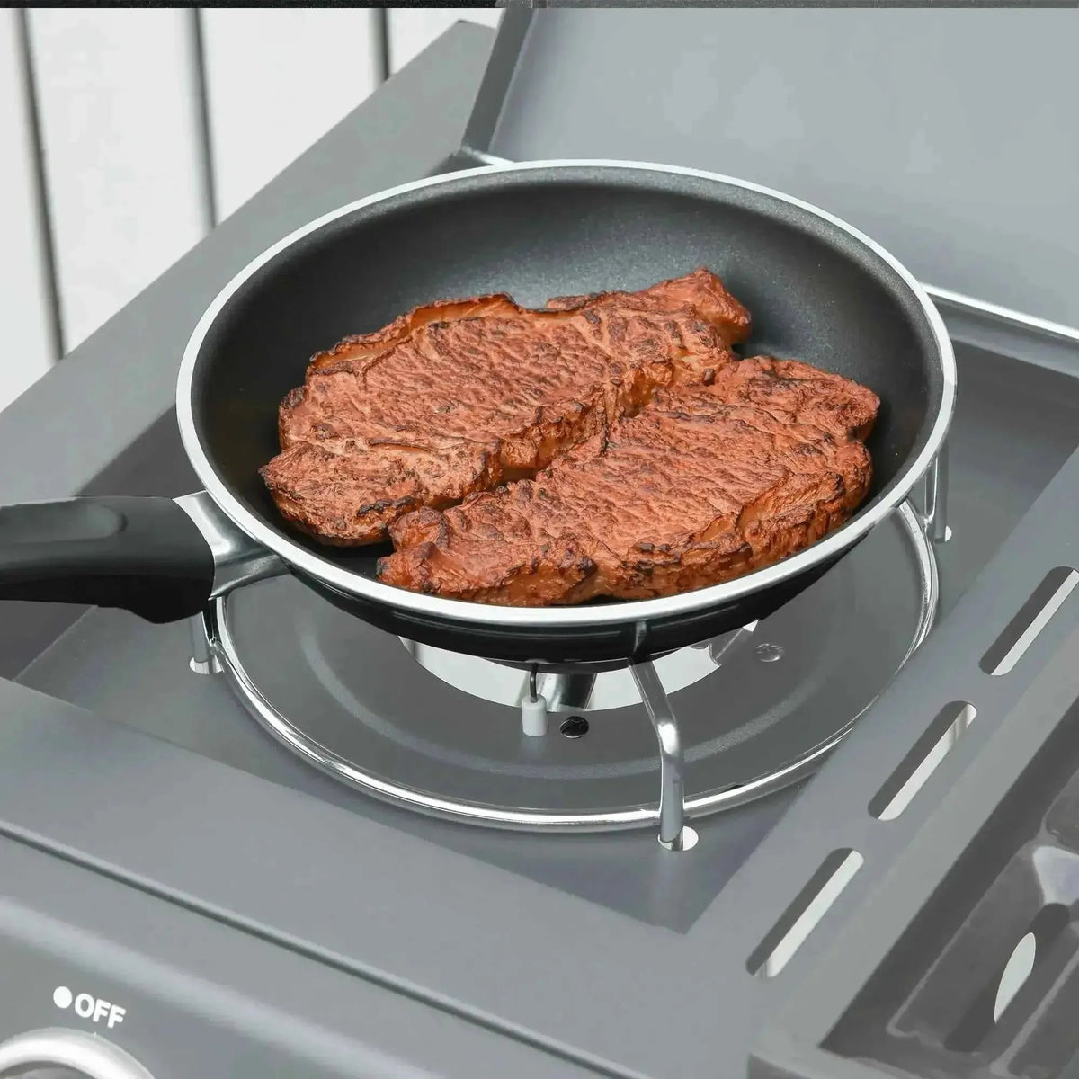 Black non-stick frying pan with black handle holding two seared steaks for use with outsunny grey gas bbq grill
