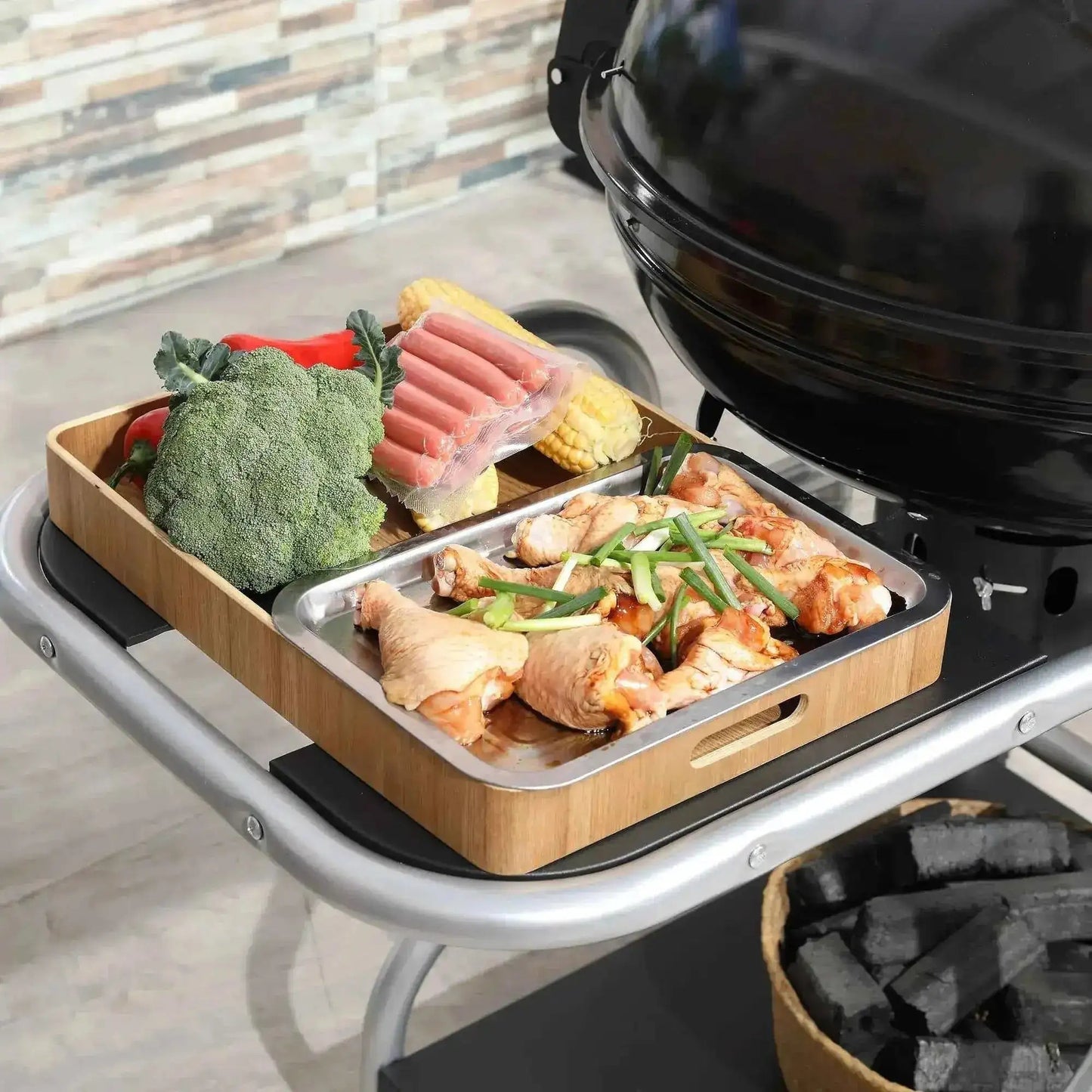 Wooden tray with stainless steel insert holding grilled chicken broccoli corn and sausages on black outsunny portable charcoal kettle grill with trolley